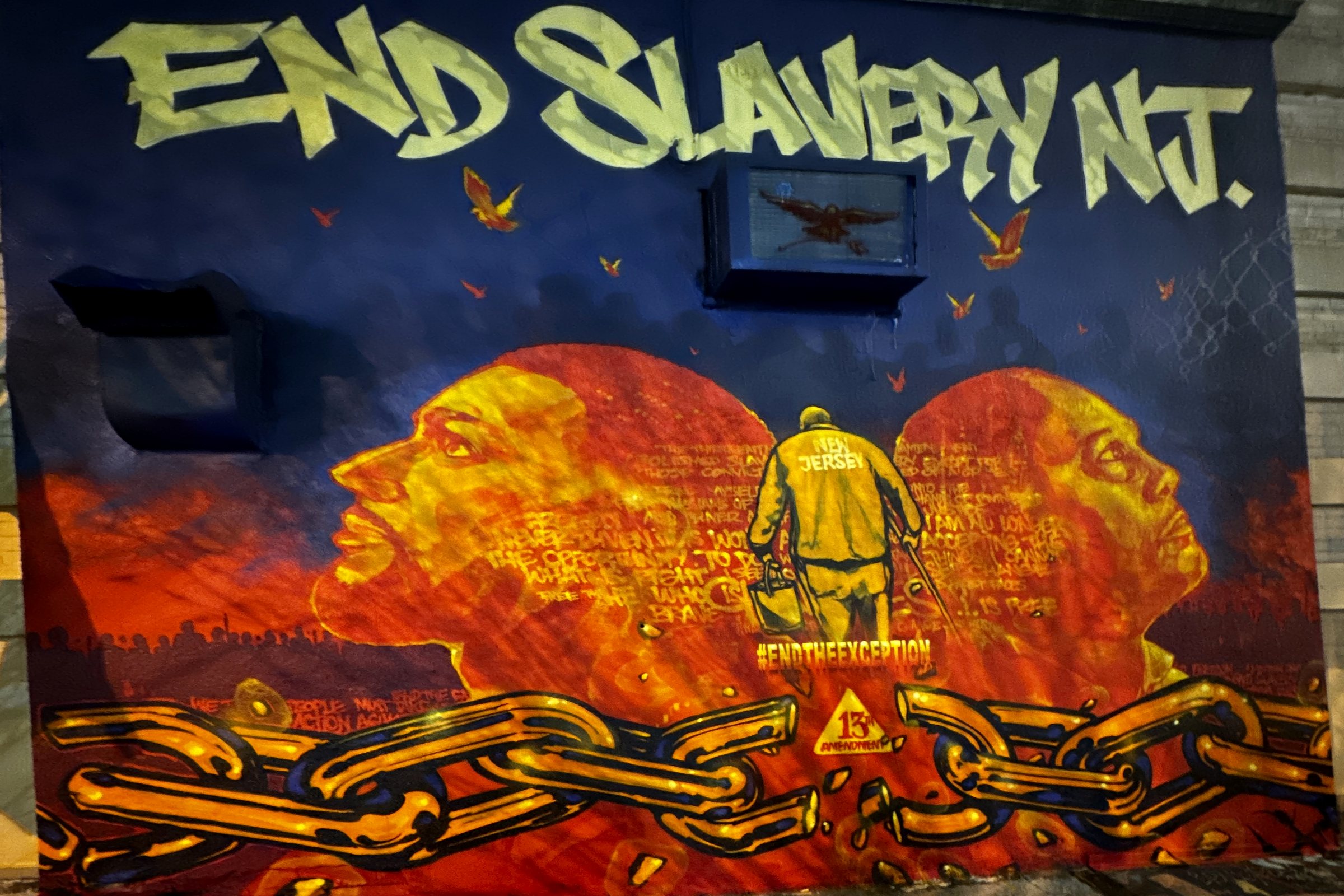 The End Slavery in New Jersey mural on a brick wall in Jersey City at night